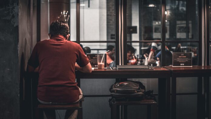 Photo by Ismail Hamzah man sitting on brown wooden bar stool beside backpack on wooden bar stool