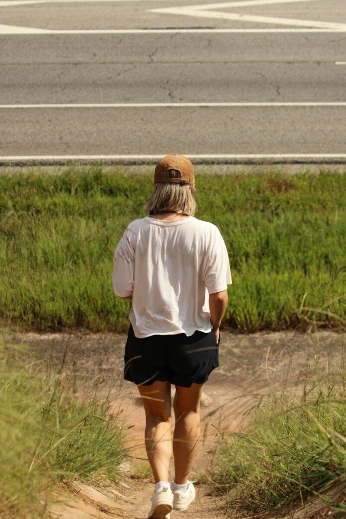 A woman walking down a dirt path next to a road
